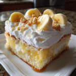 A moist slice of banana pudding poke cake topped with thick whipped cream, fresh banana slices, and crumbled vanilla wafers.
