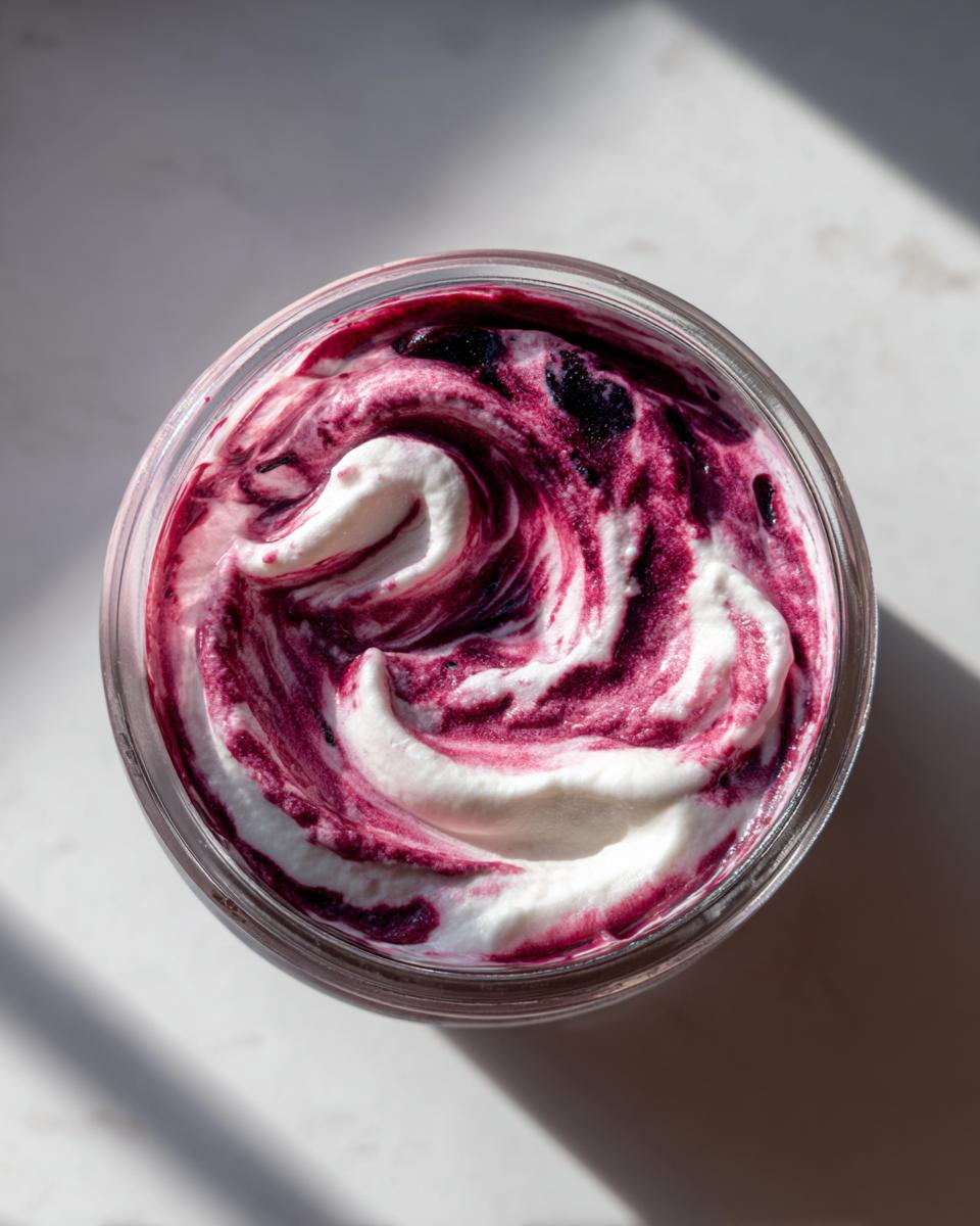 Overhead view of a berry swirl high protein cheesecake jar showing creamy white filling swirled with vibrant purple berry puree.