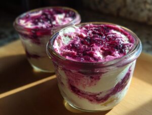 Close-up of two berry swirl high protein cheesecake jars featuring creamy white filling swirled with dark purple berry topping.