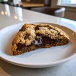 A close-up of a freshly baked chocolate chip cookie, cut in half to show the melted, gooey chocolate center.