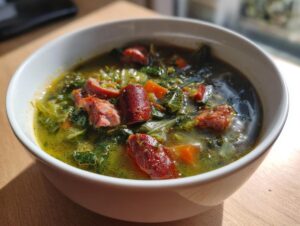 Close-up of a white bowl filled with a savory cabbage soup winter bowl featuring dark green leafy vegetables and slices of smoked sausage.