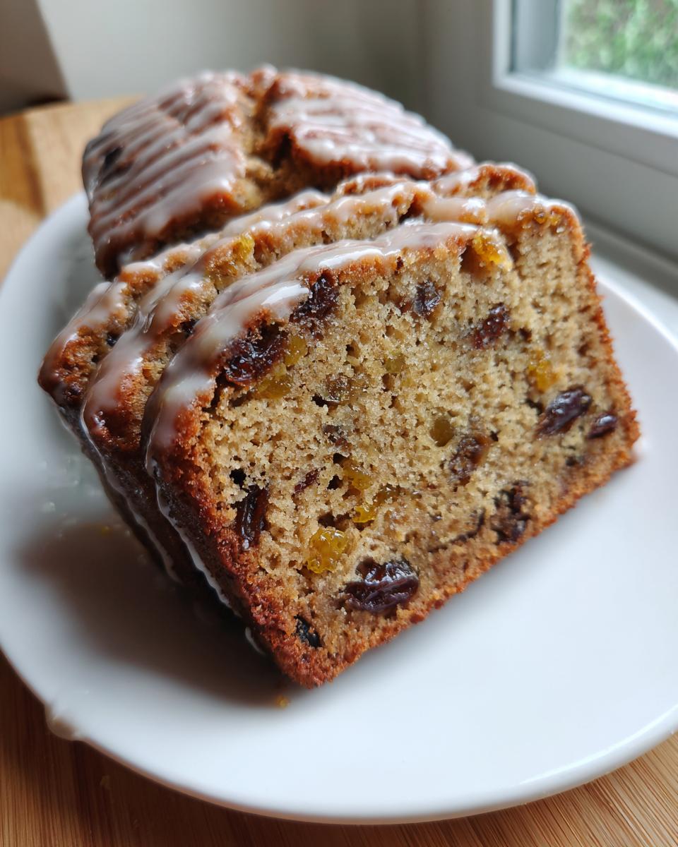 Close-up of sliced cardamom date cake drizzled with a white sugar glaze, showing dried fruit inclusions.