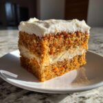 A perfect slice of carrot cake cheesecake showing layers of moist cake and cream cheese filling, topped with thick frosting.