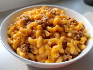 Close-up of a white bowl filled with creamy, cheesy cheeseburger pasta mixed with seasoned ground beef.