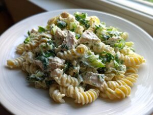 A close-up of creamy chicken caesar pasta salad featuring fusilli pasta, chunks of chicken, and chopped romaine lettuce.