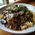 A close-up of a serving of chicken marsala casserole topped with rich mushroom sauce and parsley, served over rotini pasta.