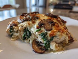 Close-up of a serving of chicken spinach mushroom low carb oven dish topped with melted, browned cheese and sliced mushrooms.