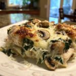 A close-up of a cheesy slice of chicken spinach mushroom low carb oven dish with browned top.