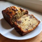 A slice cut from a loaf of moist chocolate chip protein banana bread sitting on a white plate.