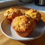 Three freshly baked citrus almond olive oil muffins topped with sliced almonds on a light plate.