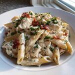 A close-up of creamy chicken bacon ranch pasta featuring penne noodles, chunks of chicken, and crispy bacon bits, topped with fresh parsley.