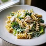 Close-up of creamy chicken caesar pasta salad featuring rotini pasta, chunks of chicken, and crisp romaine lettuce.