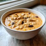 A close-up of a white bowl filled with creamy chicken taco soup, featuring chunks of chicken, corn, and black beans.