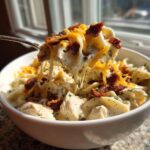 A spoonful of creamy crack chicken noodle soup being lifted, showing melted cheese, bacon, and chicken pieces.