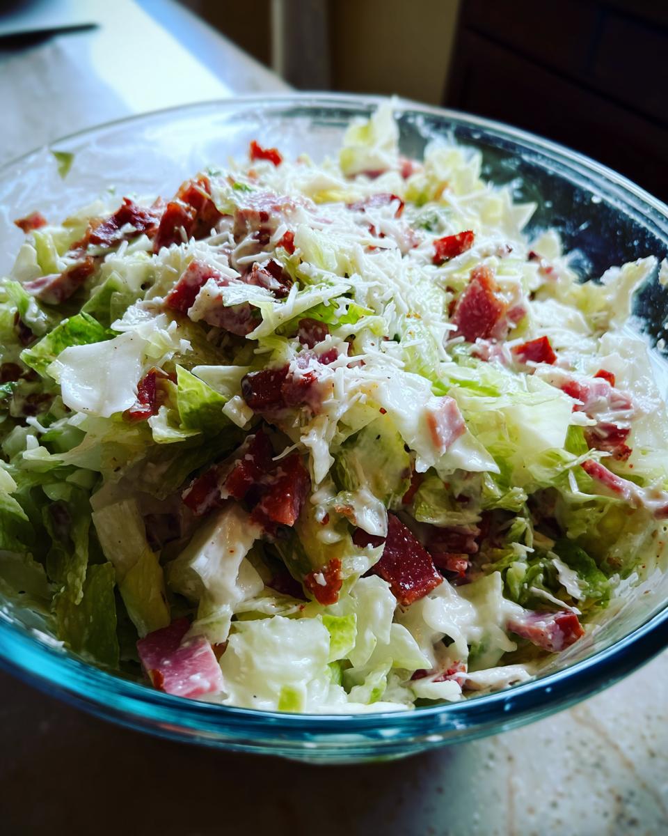Close-up of a bowl filled with creamy grinder salad featuring chopped lettuce, red meat pieces, and shredded white cheese.
