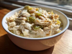 A close-up of a creamy white chicken chili recipe served in a white bowl, featuring shredded chicken, white beans, and green chilies.