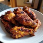 A close-up of several perfectly cooked, crispy air fryer chicken wings piled on a white plate.