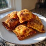 A pile of golden brown, crispy air fryer ravioli seasoned with breadcrumbs and pepper, served on a white plate.