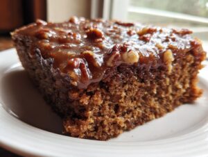 Close-up of a moist, dark slice of Dr Pepper Cake topped with a thick, glossy pecan glaze.