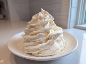 A tall, perfectly piped swirl of fluffy vanilla buttercream frosting sitting on a small white plate.