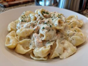 A close-up of creamy garlic butter chicken alfredo shells topped with fresh parsley in a white bowl.