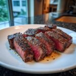 Slices of medium-rare garlic pepper steak, heavily crusted with pepper, resting on a white plate.