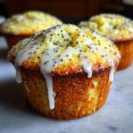 A close-up of a freshly baked lemon poppy seed muffin topped with thick white glaze and poppy seeds.