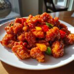 A plate piled high with crispy, glazed pieces of sweet and sour chicken mixed with chunks of red pepper and pineapple.