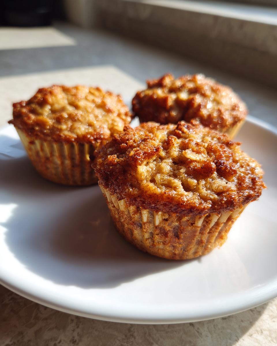 Three golden-brown banana oatmeal cups sitting on a white plate, highlighted by strong natural sunlight.