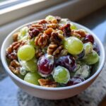 A white bowl filled with creamy grape salad featuring green and red grapes topped generously with candied walnuts.