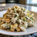 Close-up of a creamy mound of chickpea chicken salad mixed with whole chickpeas and fresh dill, served on a white plate.