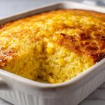 Close-up of a freshly baked Jiffy corn casserole with a golden crust in a white baking dish.