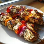 Close-up of several juicy chicken kebabs seasoned with herbs, grilled with red onion and bell peppers.