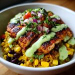 A close-up of a vibrant lemon chili grilled chicken bowls featuring seasoned chicken over yellow rice with corn and black beans, topped with salsa and green sauce.