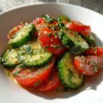Close-up of a vibrant marinated cucumber tomato salad, glistening with dressing and topped with fresh dill.
