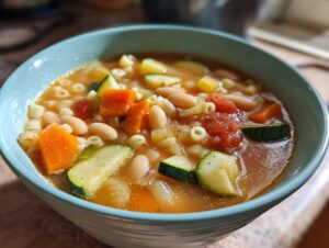 Close-up of a light blue bowl filled with vibrant minestrone soup featuring beans, carrots, zucchini, and pasta.