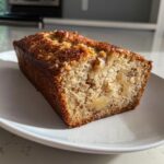 Close-up of a moist slice of hawaiian banana bread showing nuts and banana chunks inside.