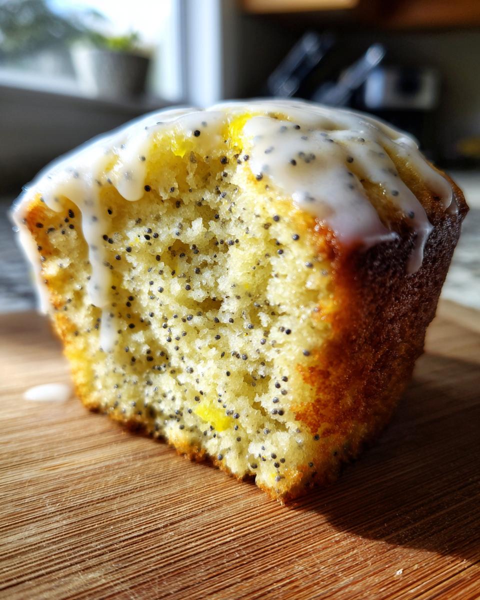 Cross-section view of a moist lemon poppy seed muffin topped with a thick, white lemon glaze.