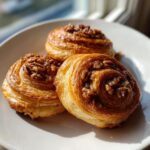 Three golden brown pecan pie crescents with sticky pecan topping resting on a white plate.