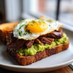 A delicious open-faced prime rib and eggs avocado toast topped with a sunny-side-up egg.