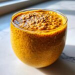 Close-up of vibrant orange pumpkin spice chia seed pudding in a clear glass, topped with chia seeds.