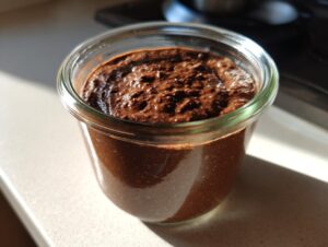 Close-up of thick, rich chocolate overnight oats in a small glass jar, illuminated by sunlight.