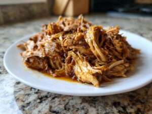 A pile of shredded, seasoned chicken meat, ready for slow cooker chicken gyros, served on a white plate.