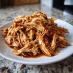 A mound of seasoned, shredded chicken, perfect for slow cooker chicken gyros, resting on a white plate.