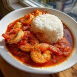 A white bowl filled with vibrant red shrimp creole sauce, plump shrimp, and a mound of white rice.