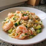 A close-up view of a bright shrimp orzo salad featuring large pink shrimp, diced cucumber, feta cheese, and fresh parsley.