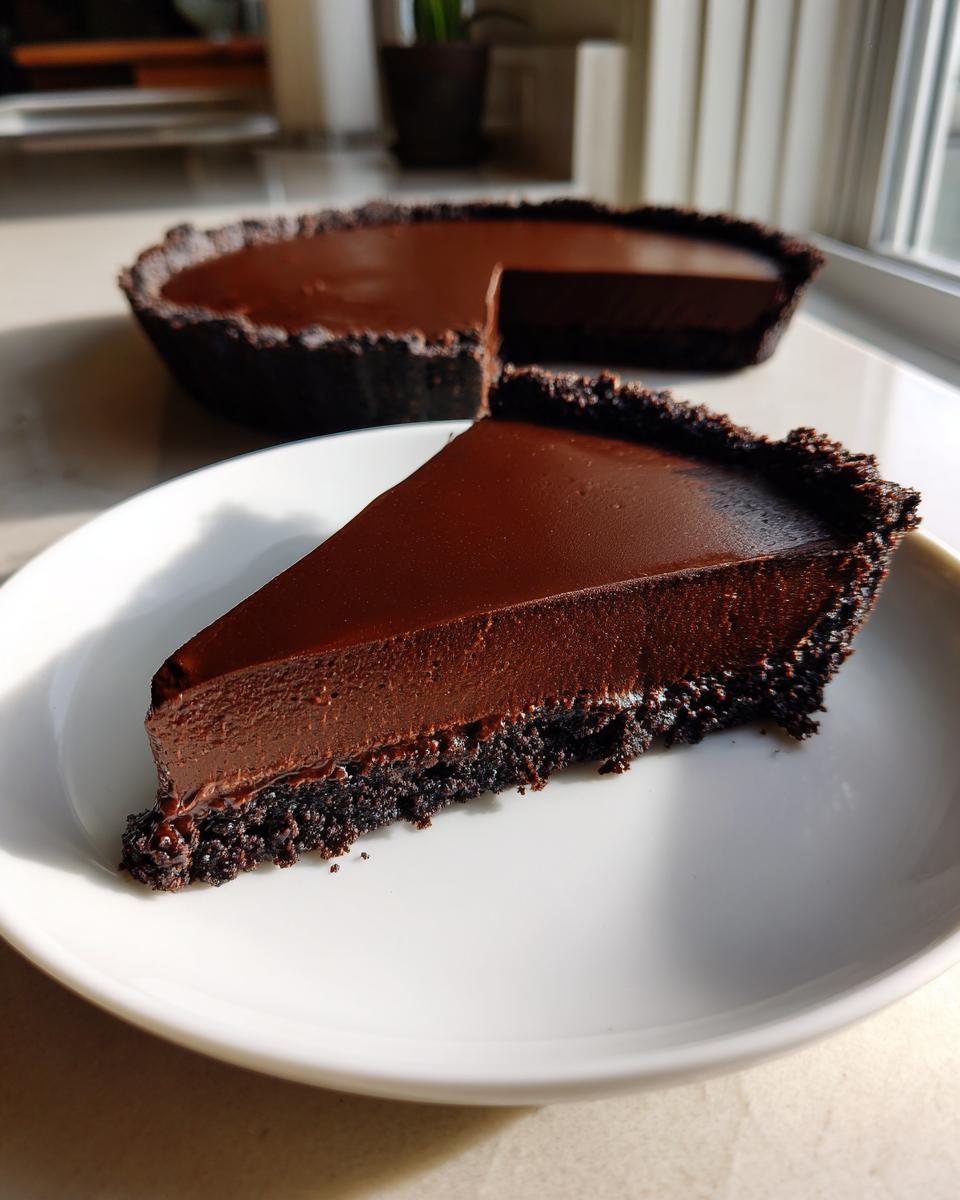 A perfect slice of decadent chocolate fudge pie with a dark, crumbly crust served on a white plate.