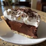 A close-up of a decadent slice of french silk pie featuring rich chocolate filling, topped with whipped cream and chocolate shavings.