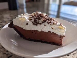 A decadent slice of french silk pie featuring a dark chocolate filling, whipped cream topping, and chocolate shavings.
