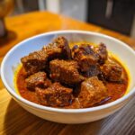 Close-up of tender chunks of meat in a rich, red sauce, representing the slow cooker lamb curry, with steam rising.